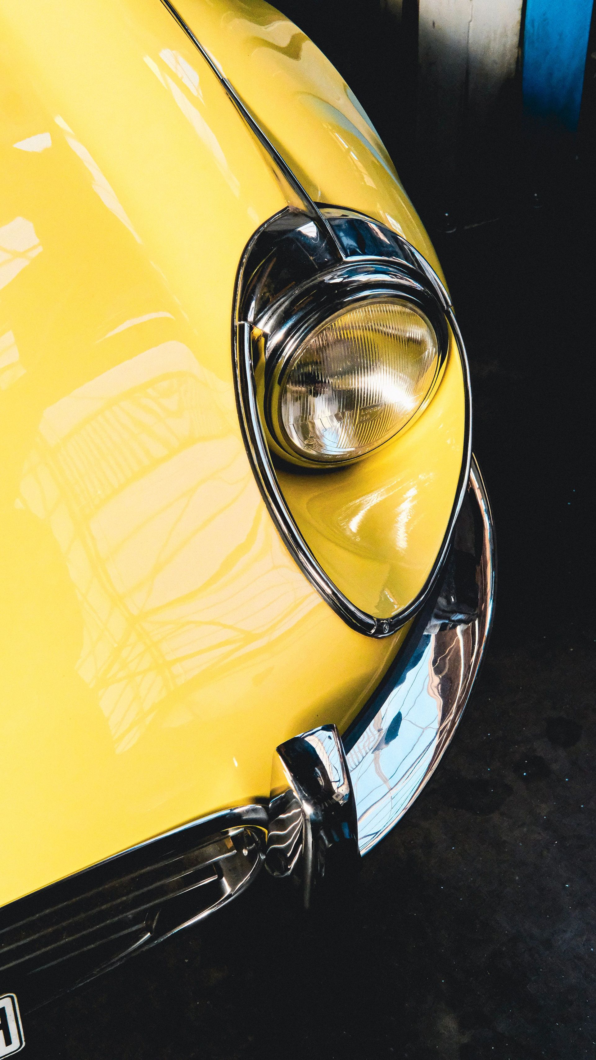 Close-up of a classic yellow car with chrome details and reflection in sunlight.